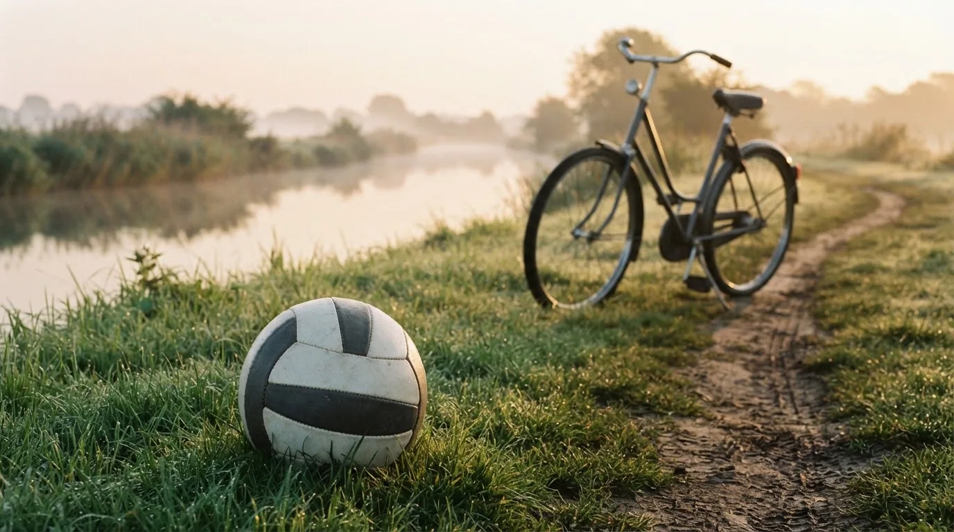 Ein Fussball liegt auf einer Wiese neben einem Fahrrad, im Hintergrund ein Kanal im Morgenlicht