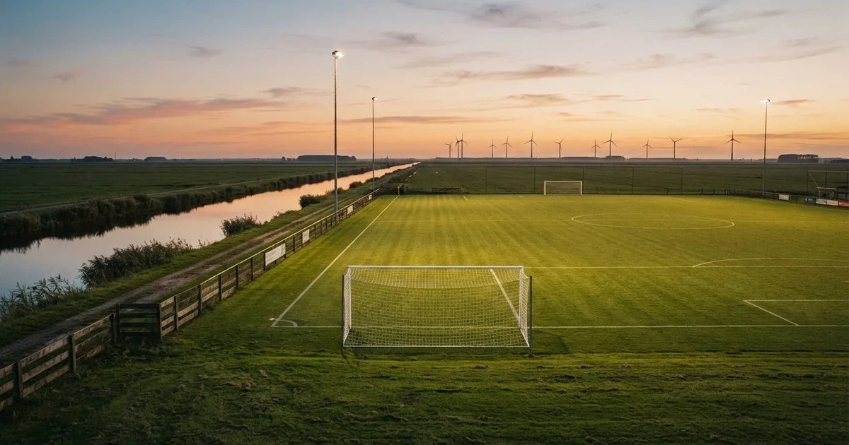 Ein Fussballplatz neben einem Kanal in flachem Land mit Windrädern am Horizont, Abendlicht liegt über dem Rasen